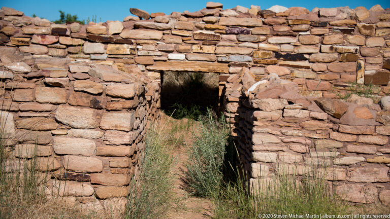 A low doorway with a stone lintel opens through a thick pueblo wall.