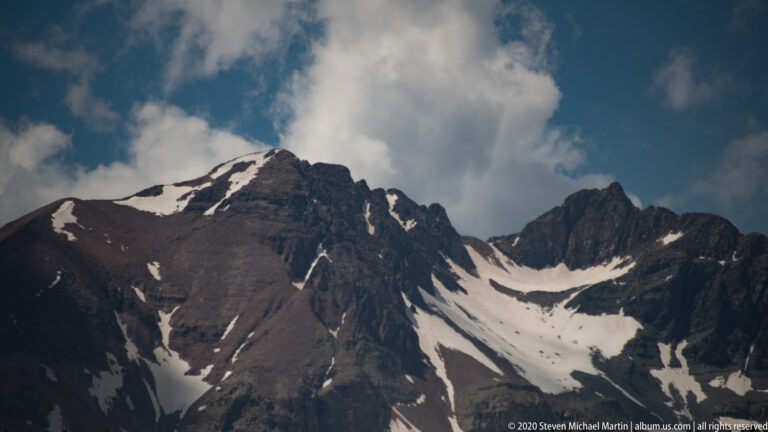 Narrow snowfields cut through steep dark rock gullies across a close mountain view.