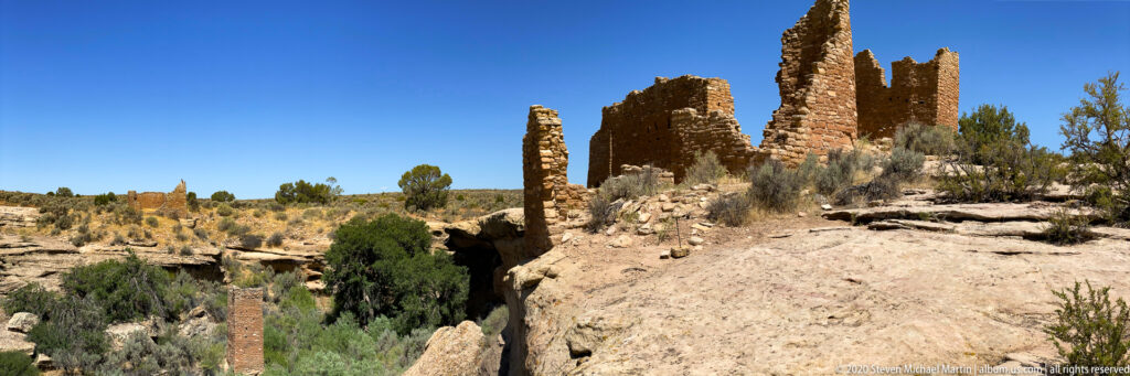Masonry towers rise beside a deep sandstone cleft, with shrubs across the rim and canyon floor.
