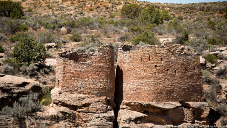 Two rounded stone structures stand on a sandstone shelf above a dark fissure.