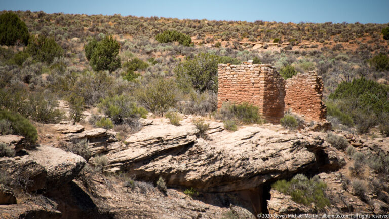 Two narrow masonry towers stand beyond layered slickrock, above a shadowed fissure.
