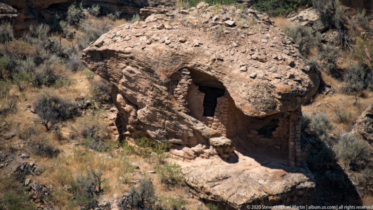 A broad sandstone caprock shelters a masonry room with a deep dark entrance.