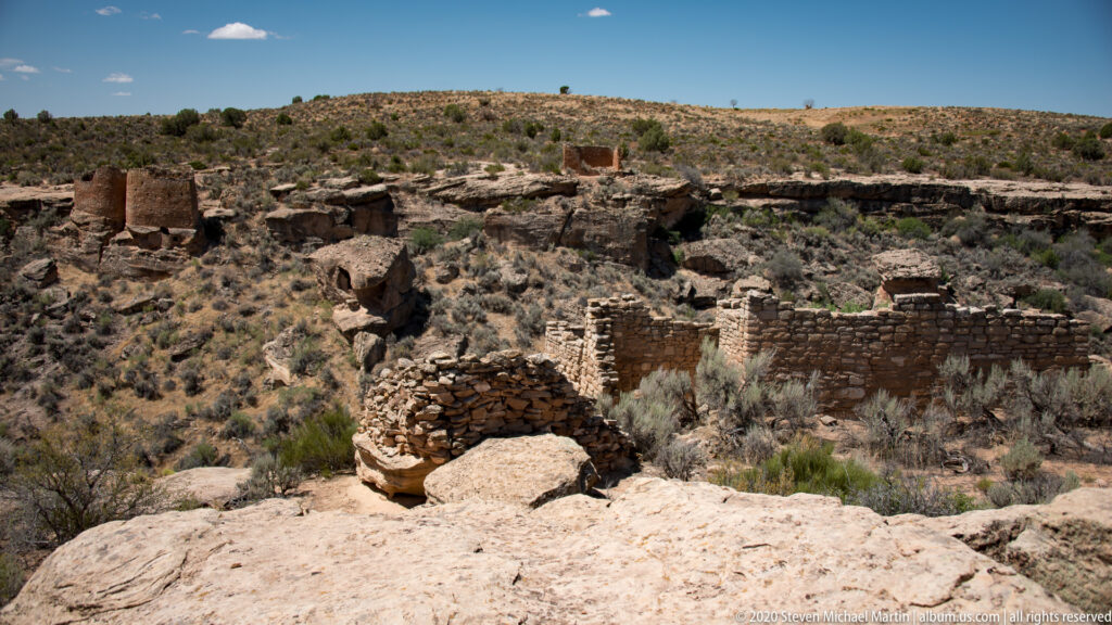 Low stone walls and partial rooms spread across a sandstone shelf below distant mountains.