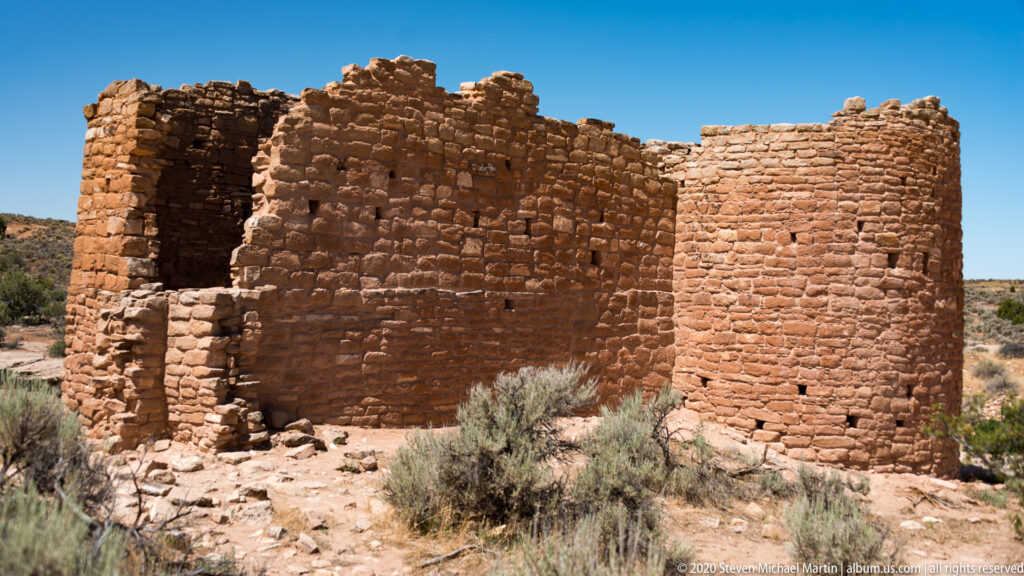Close sandstone walls show small openings, a dark recess, and a rounded tower end.