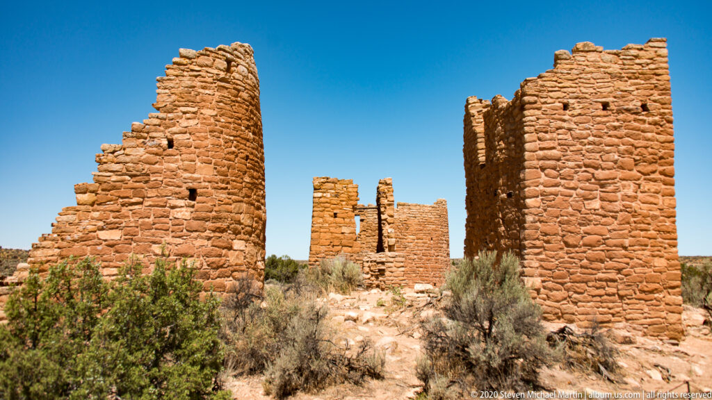A rocky passage runs between two tall sandstone walls toward additional masonry structures.