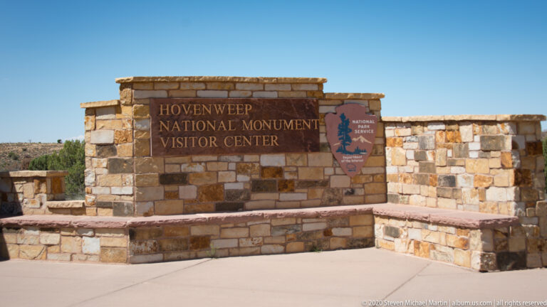 A stone entry wall names the Hovenweep National Monument Visitor Center and displays an NPS emblem.