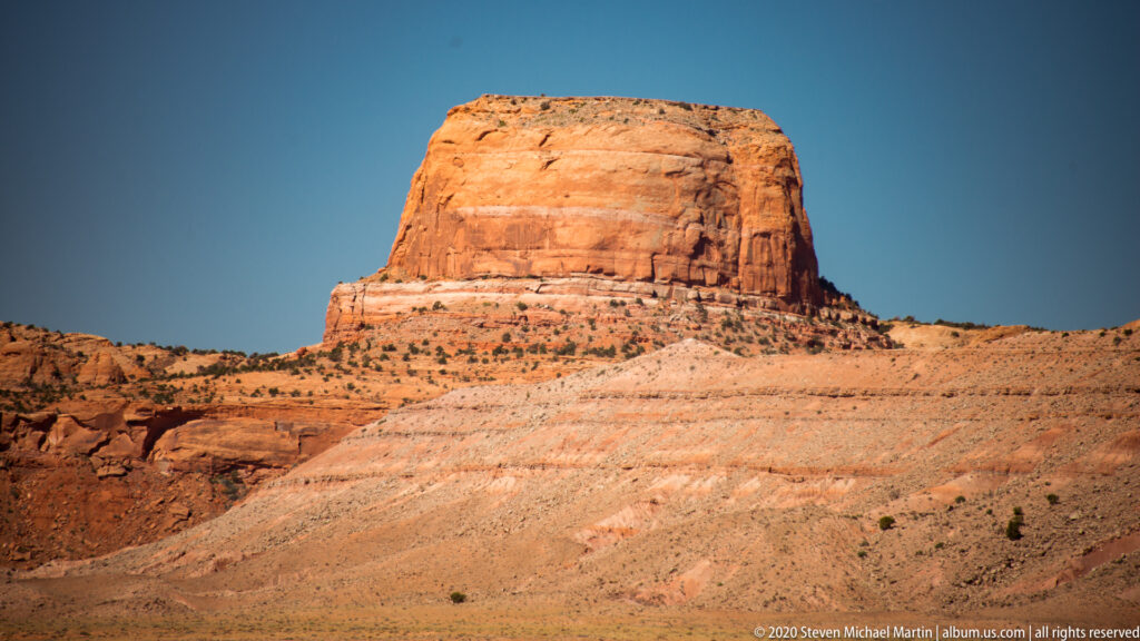 A broad orange mesa has a vertically grooved face above a pale sloping rock apron.