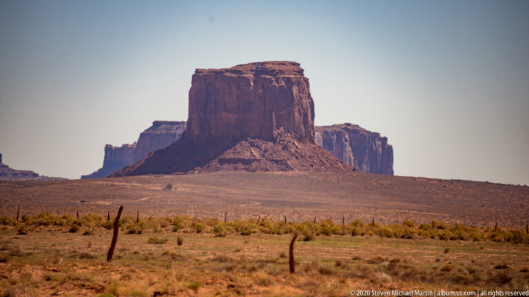 A broad flat-topped butte stands beyond a dry scrub plain with layered mesas behind.
