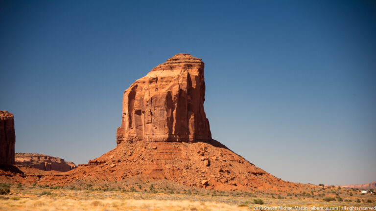 A sheer orange butte with vertical grooves rises above a sloping talus apron.
