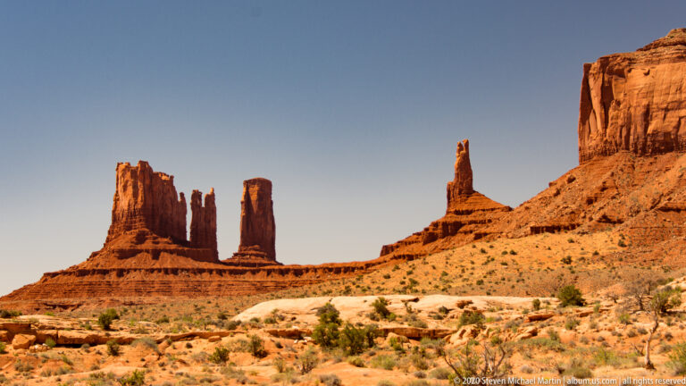 Several narrow red spires stand along a ridge beneath a larger cliff at right.