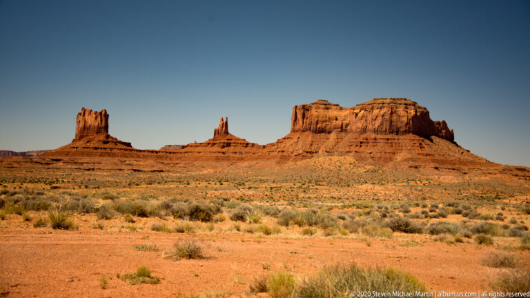 A line of red buttes and spires stands beyond a broad, shrub-dotted plain.