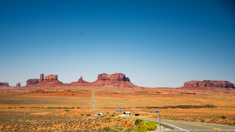 A straight highway crosses the basin toward distant red buttes and mesas.