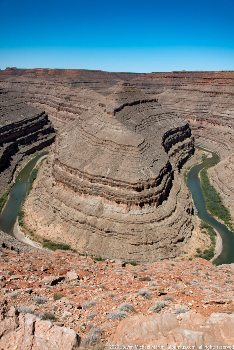 The San Juan River loops around a striped rock promontory inside a steep canyon.