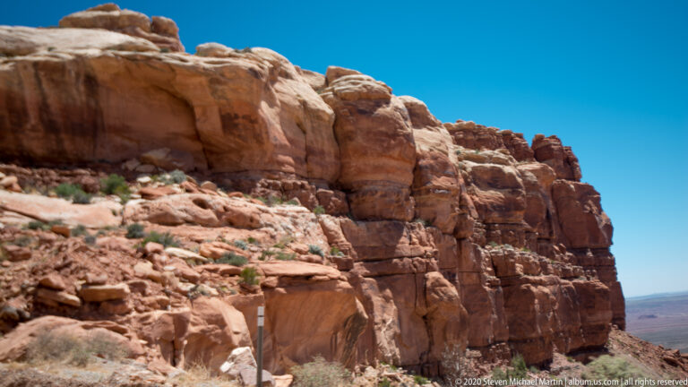 A broad dark arch opening cuts through the base of a tall red sandstone cliff.