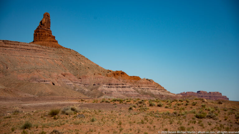 A small flat-topped tower rises from a layered ridge above a scrub-covered slope.