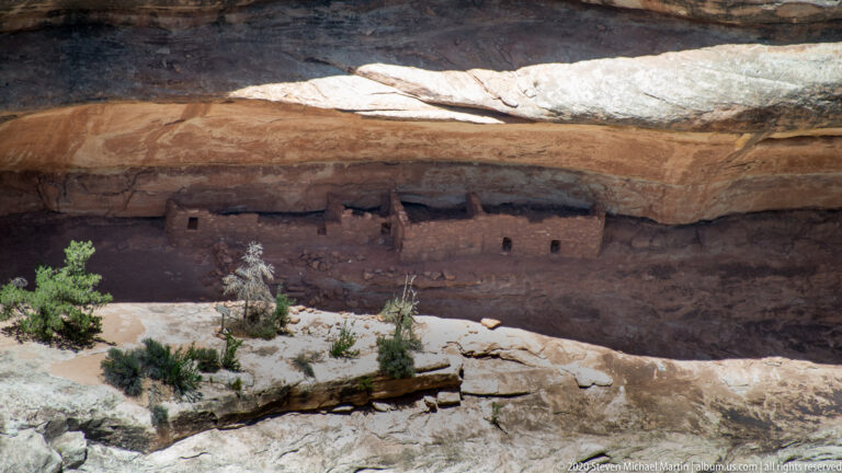 Low stone rooms with small openings sit beneath a pale overhanging sandstone roof.