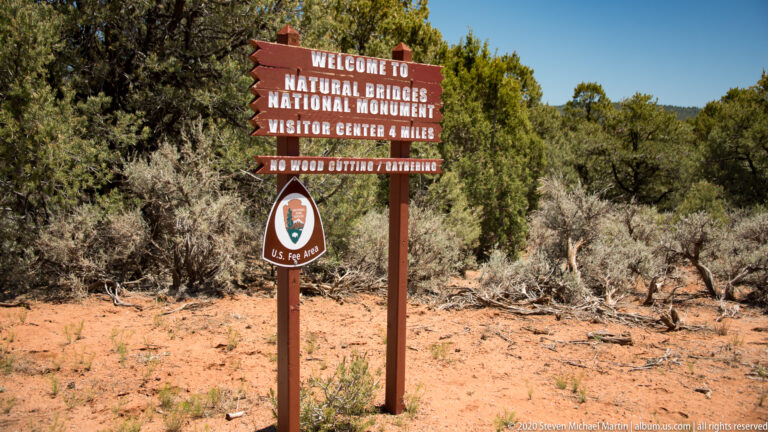 A welcome sign names Natural Bridges National Monument and points four miles to its visitor center.