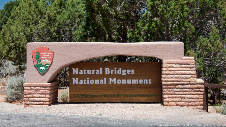 A masonry entrance marker names Natural Bridges National Monument and displays the National Park Service emblem.