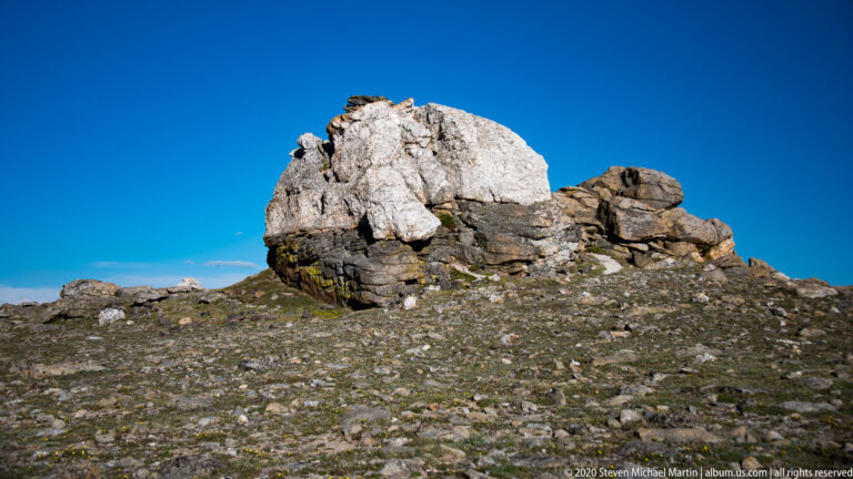 Pale granite caps darker blocky rocks on a barren summit beneath a deep blue sky.