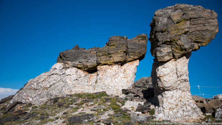 Two pale rock pillars support broad dark capstones against a clear blue sky.