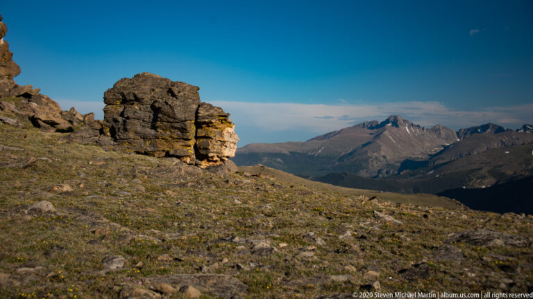 Granite outcrop at left overlooks a meadow slope and distant mountain range.