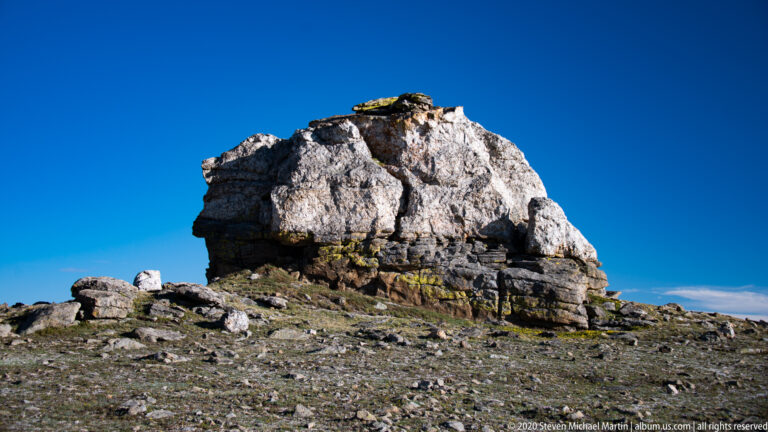 Small dark bird perches atop a pale granite block against open sky.