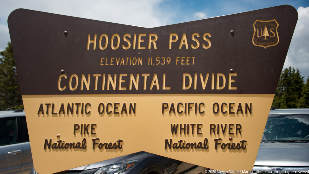 A sign names Hoosier Pass, its elevation, the Continental Divide, and two national forests.