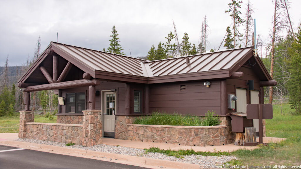 A low timber park building with a metal roof and stone base stands beside a road.