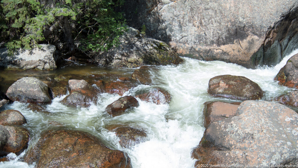 Whitewater rushes between rounded granite boulders and spills into a darker pool.