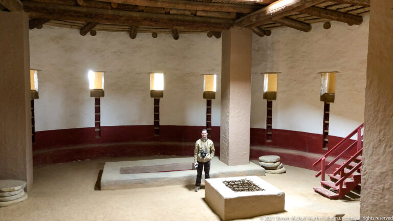 Elevated view of a visitor standing near the central feature and stairs inside the reconstructed Great Kiva.