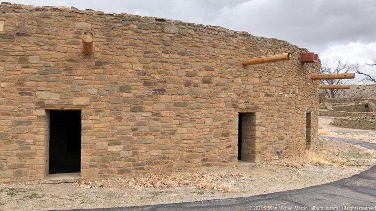 Stone masonry exterior with two rectangular doorways and round roof timbers projecting from the upper wall.