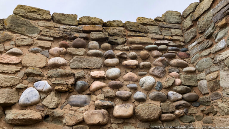 Close view of rounded multicolored river cobbles set as a patterned panel within rough stone masonry.