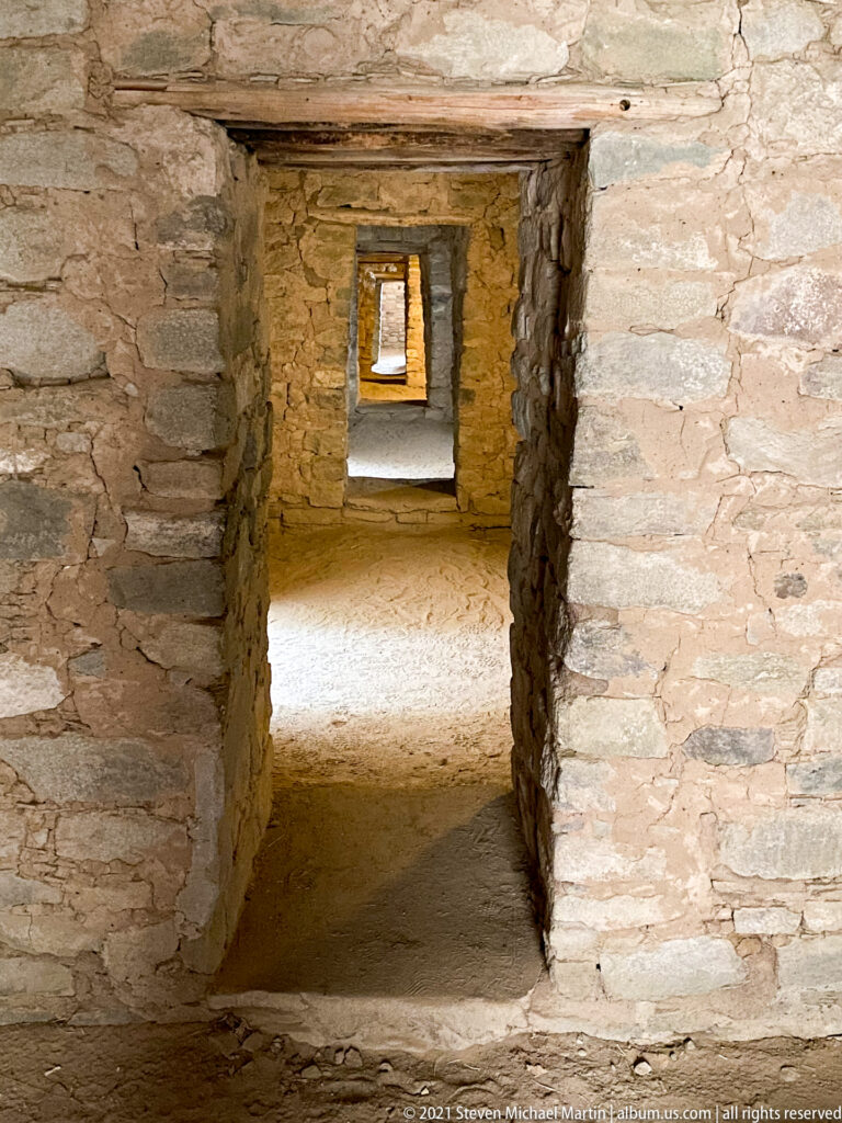 Low aligned doorways recede through several connected stone rooms toward a bright opening.