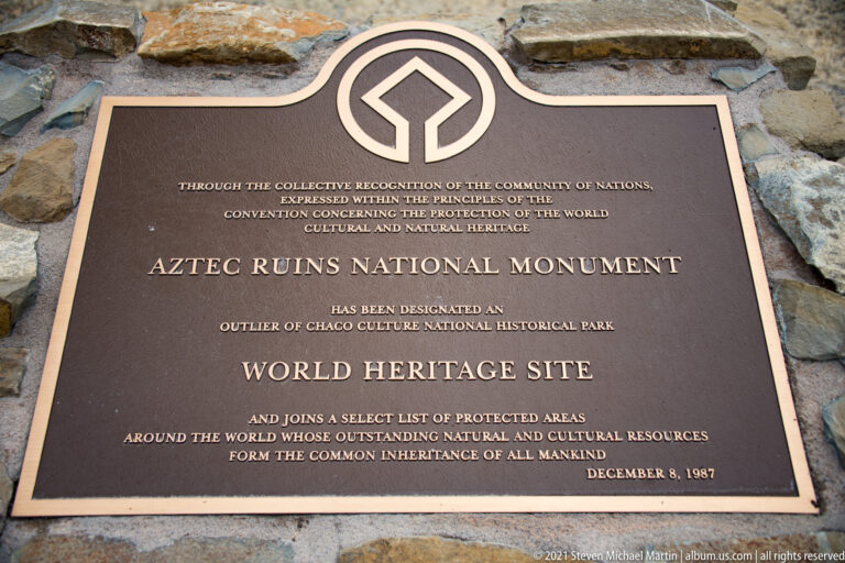 Bronze World Heritage Site plaque for Aztec Ruins National Monument mounted on a rough stone wall.