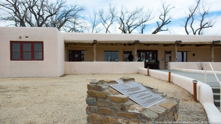 World Heritage plaque on a stone pedestal in front of the low stucco visitor center and timber porch.