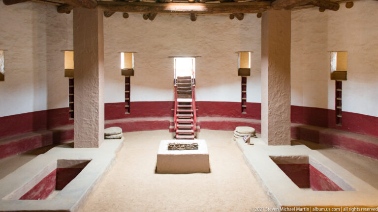 Symmetrical Great Kiva interior with central ladder, masonry floor feature, paired recesses, and large supports.