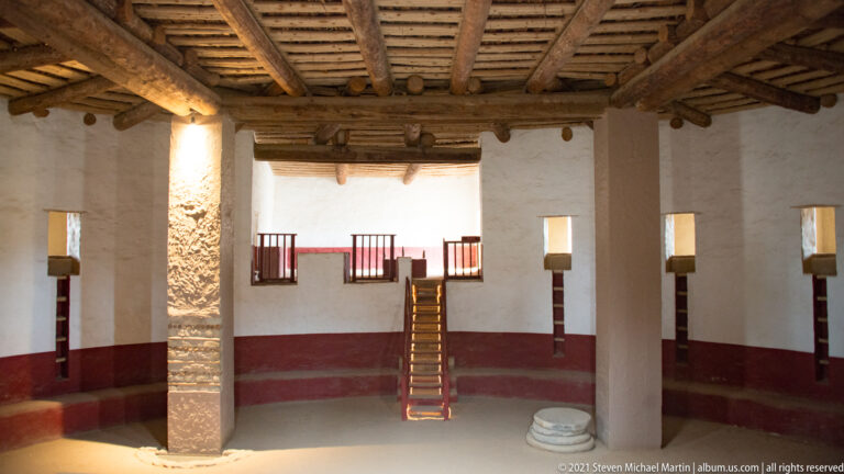Heavy timber ceiling and square supports above the ladder and plastered walls of the reconstructed Great Kiva.