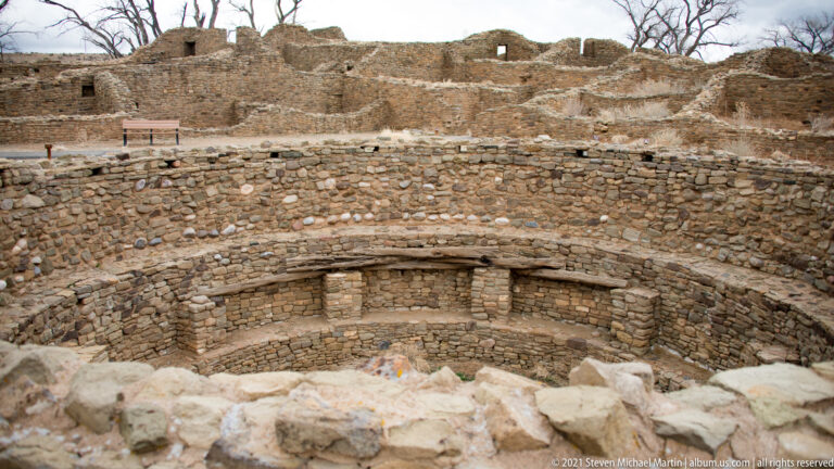 Close elevated view into a circular kiva with concentric masonry ledges, rectangular recesses, and lower central floor.