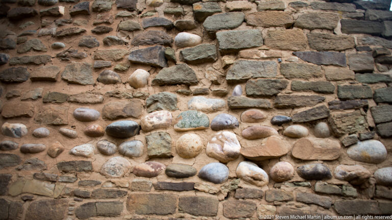 Close masonry detail with rounded multicolored cobbles set among flatter coursed stones.