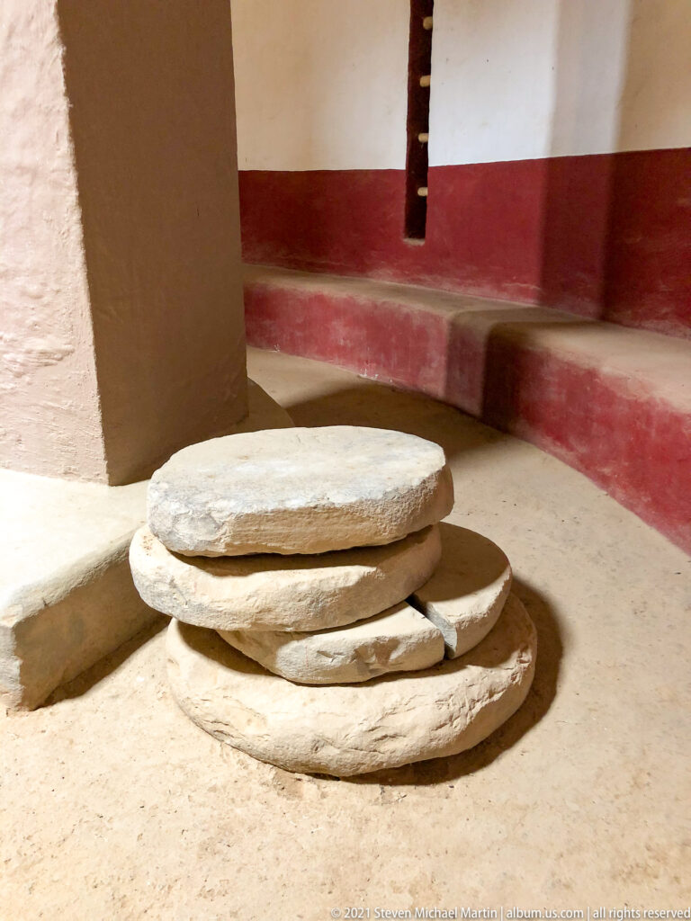 Several flat circular stone slabs stacked on the floor beside a large support in the reconstructed Great Kiva.