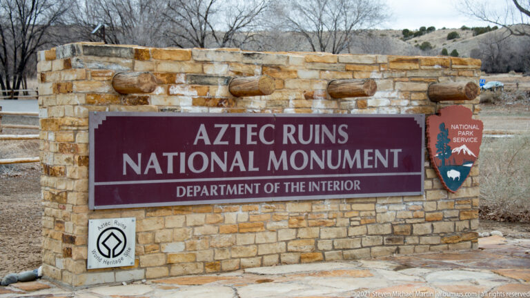 Maroon Aztec Ruins National Monument sign in a stone frame with National Park Service arrowhead and World Heritage emblem.