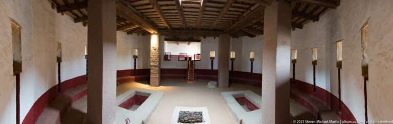 Elevated view into the reconstructed Great Kiva with square supports, ladder, red wall band, floor recesses, and central feature.
