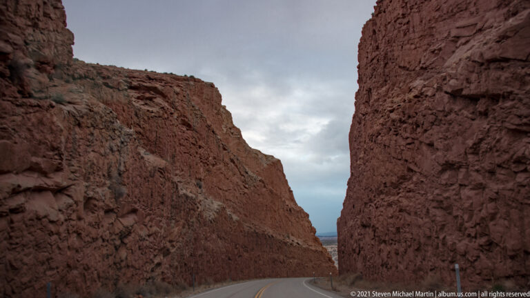 A paved road passes through a narrow corridor between tall red sandstone walls.