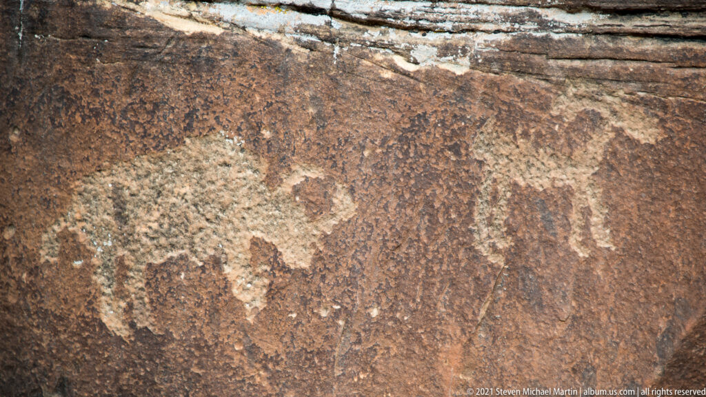 A dark animal-like outline sits beside a pale weathered patch on a sandstone panel.