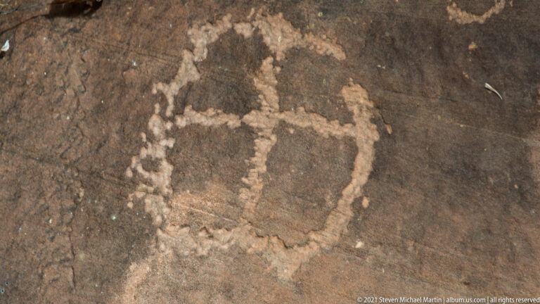 A pale rectangular petroglyph with a narrow upper extension is centered on dark stone.