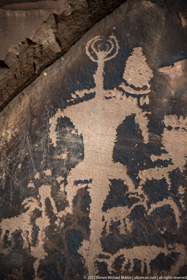 A large pale petroglyph lies below a ring-shaped motif on an angled sandstone panel.