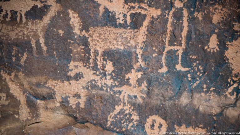 Pale outlines and abstract marks form a dense cluster across an uneven dark rock face.