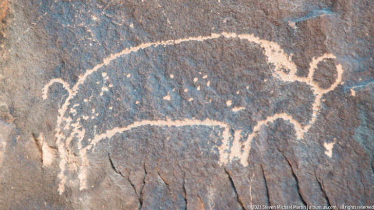 A broad animal-like petroglyph with a curved extension appears beside a small circular mark.