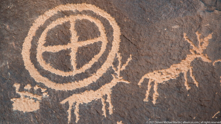 A divided circular petroglyph sits above a row of small animal-like outlines on dark stone.