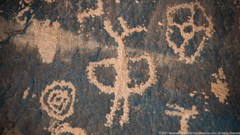 A circular motif and several upright forms appear together on cracked dark sandstone.